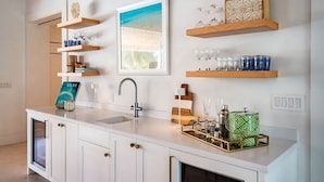 Una cucina moderna con mobili bianchi, un lavello incassato e scaffali in legno con bicchieri e oggetti decorativi.