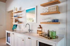 Une cuisine moderne avec des meubles blancs, un évier encastré et des étagères en bois où sont exposés de la verrerie et des objets décoratifs.