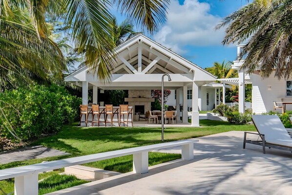 A modern outdoor patio with a dining area, surrounded by lush greenery and palm trees.