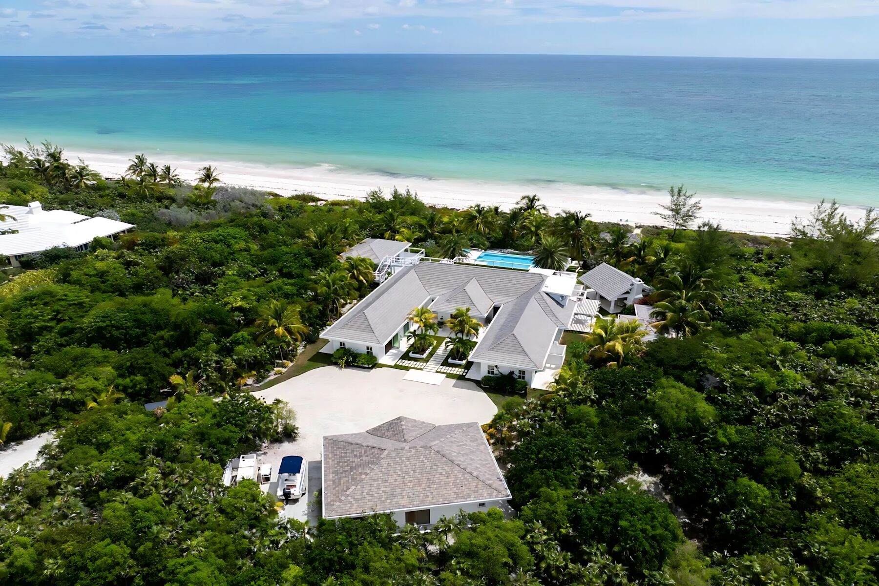 An aerial view of a coastal property with multiple buildings, a swimming pool, and a beach.