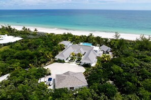 An aerial view of a coastal property with multiple buildings, a swimming pool, and a beach.
