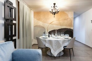 A dining area with a round table set for four, a chandelier, and a wall with a textured mural. - MALVASIA SUITE (Venezia)