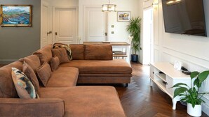 A living room with a brown sectional sofa, a dining table, a TV, and a potted plant. - Our Cosy Cottage in Gatehouse of Fleet (Gatehouse of Fleet)