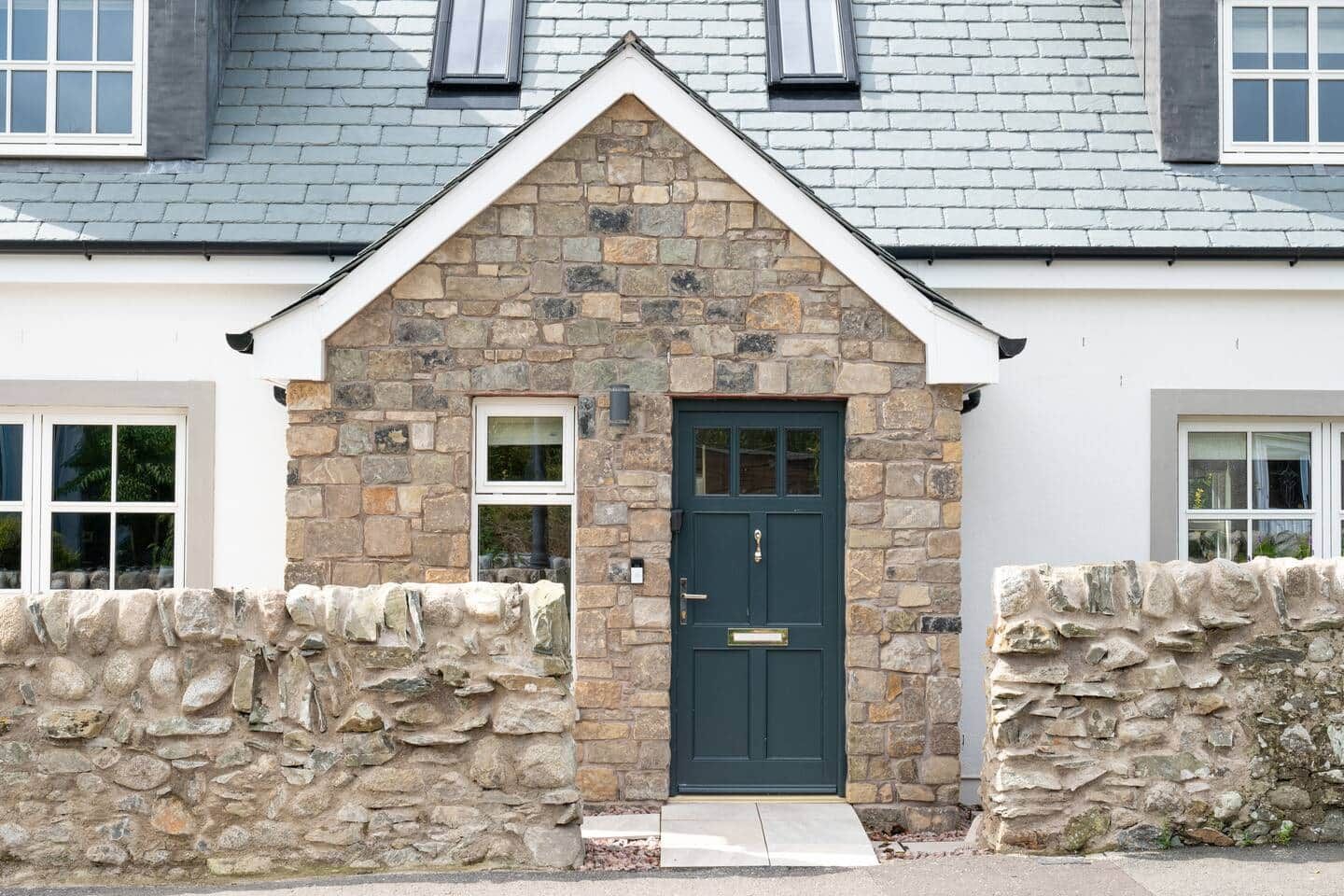 A stone facade with a dark green door, a small window, and a stone wall.
