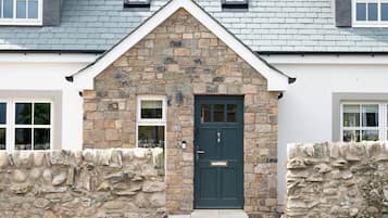 A stone facade with a dark green door, a small window, and a stone wall.