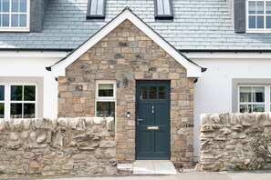 A stone facade with a dark green door, a small window, and a stone wall. - Our Cosy Cottage in Gatehouse of Fleet (Gatehouse of Fleet)