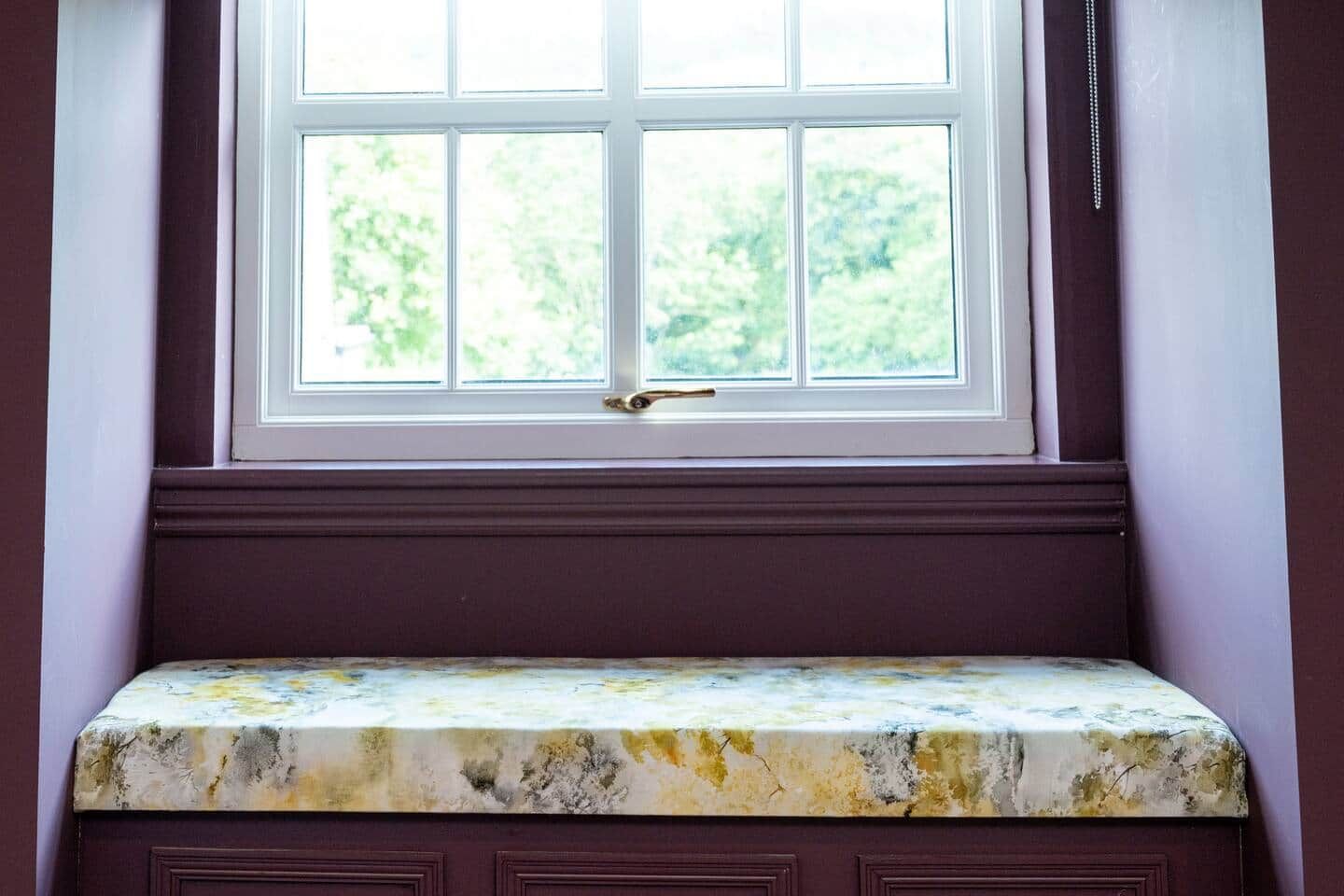 A window with a view of greenery, a bench with a marble-like surface, and a door with a brass handle.