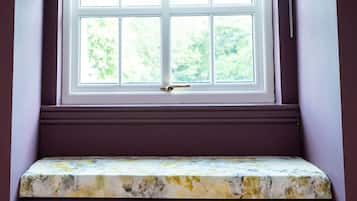 A window with a view of greenery, a bench with a marble-like surface, and a door with a brass handle.