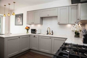 Une cuisine moderne avec des meubles gris, un plan de travail blanc, un four à micro-ondes, un évier avec des robinets dorés et une cuisinière.