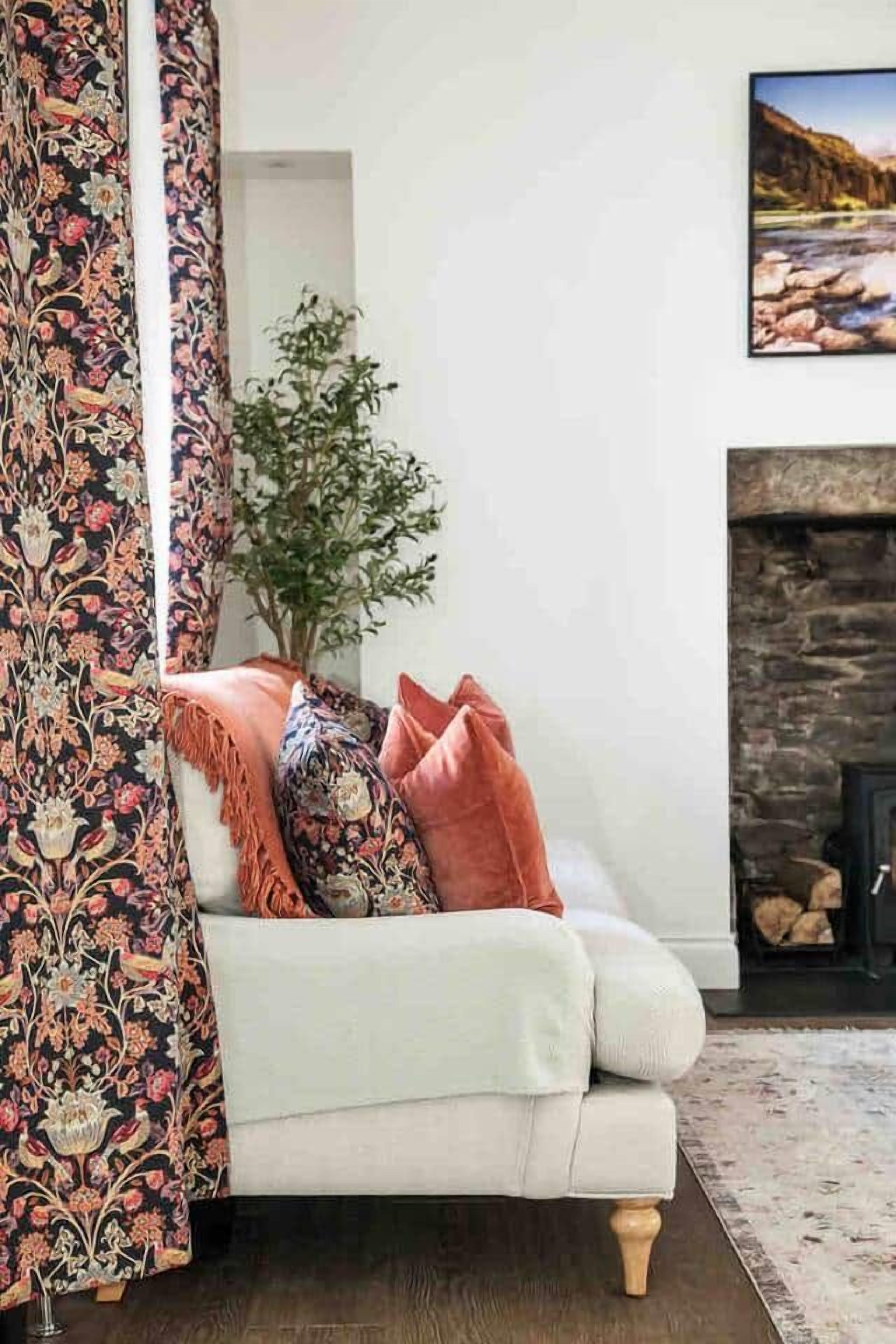 A living room with a sofa, a fireplace, a plant, and a painting on the wall.