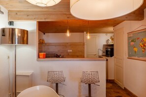 A kitchen with wooden beams, hanging light fixtures, a stainless steel refrigerator, and a world map on the wall. - Le Cocon – Cozy Village House with Mountain Views (Puimoisson)