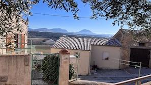 A rural house with a tiled roof, a small garden, and a view of distant mountains. - Le Cocon – Cozy Village House with Mountain Views (Puimoisson)