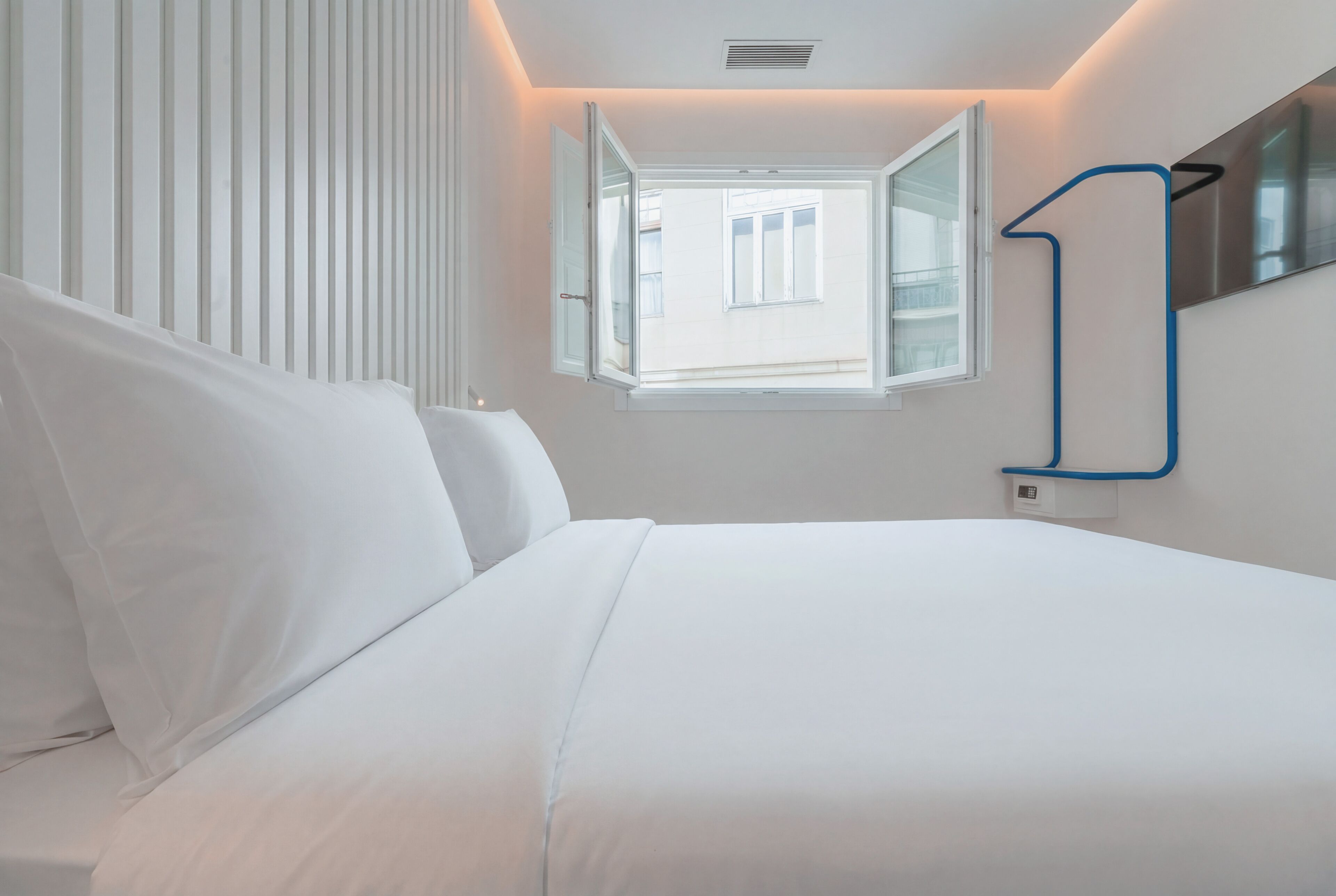 Un dormitorio moderno con una cama grande, una ventana y un estante azul montado en la pared.