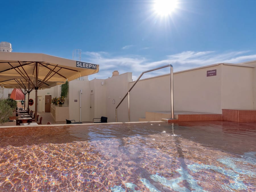 Un área de piscina en la azotea con una sombrilla que dice 'SLEEPN' y una escalera que lleva a un nivel superior.