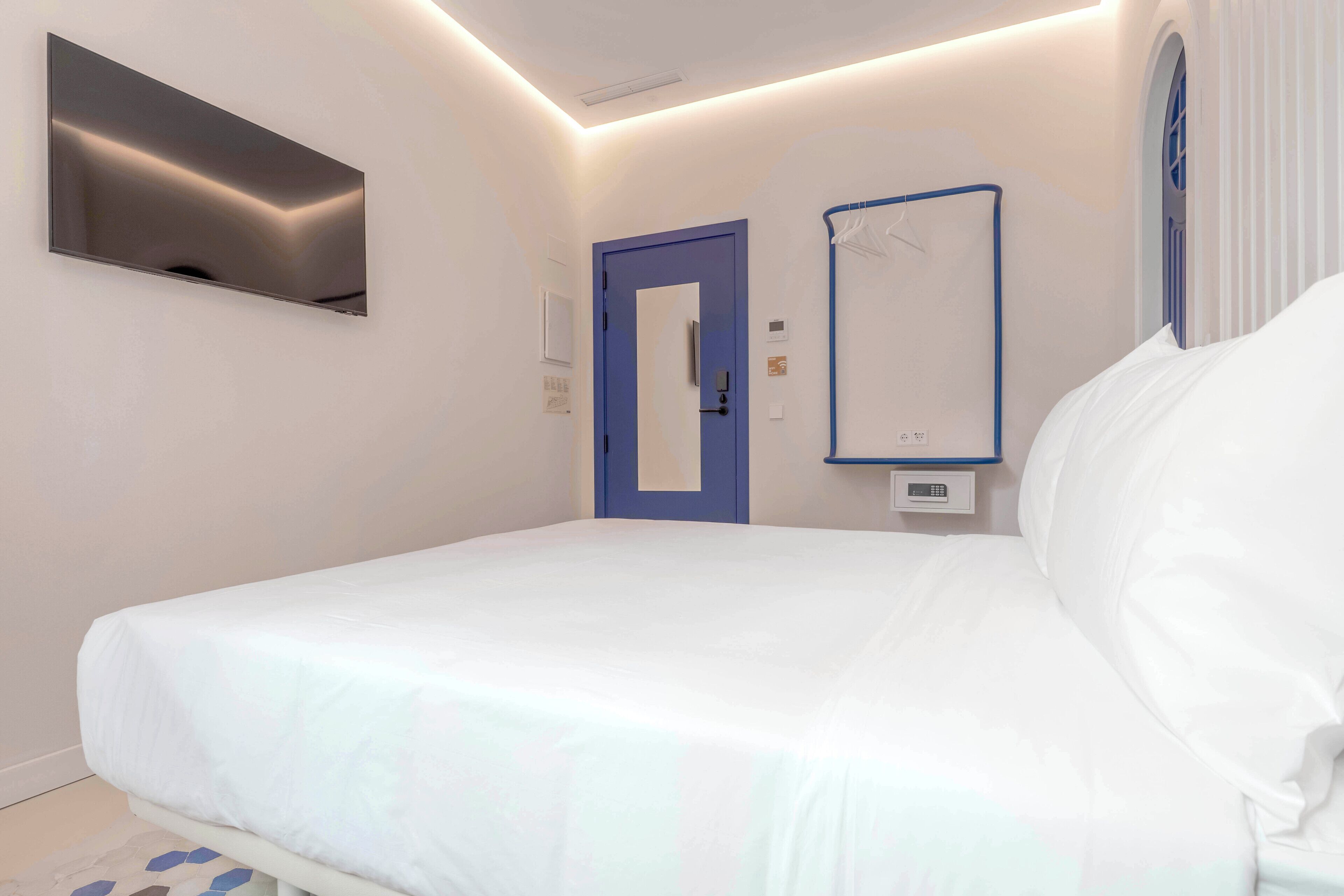 Een slaapkamer met een bed, een blauwe deur, een spiegel en een aan de muur bevestigde televisie.