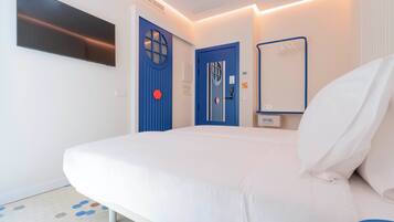 A hotel room with a bed, two doors, a mirror, and a flat-screen TV mounted on the wall.