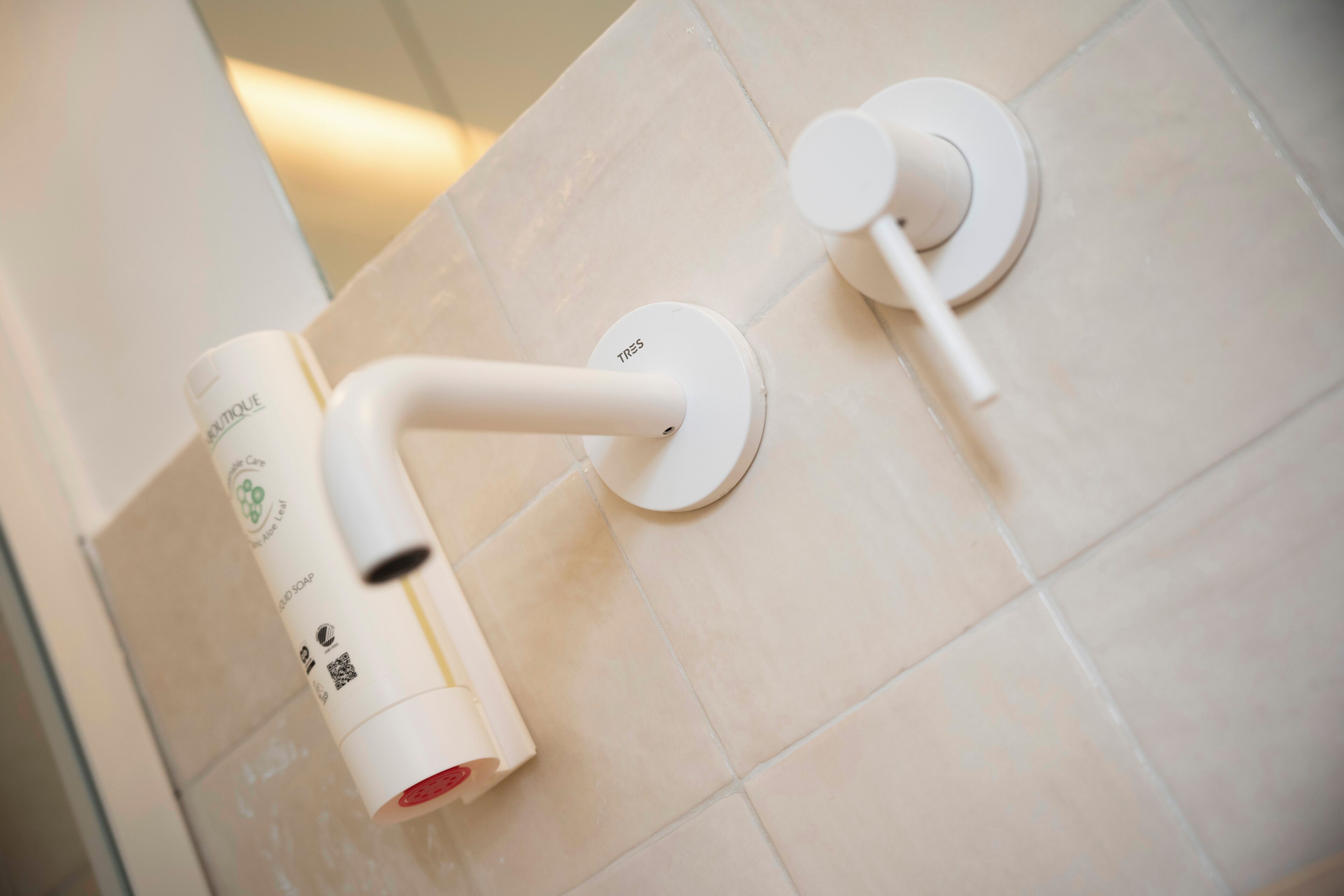 Une salle de bain équipée d’un distributeur de savon liquide et d’un robinet fixé au mur.