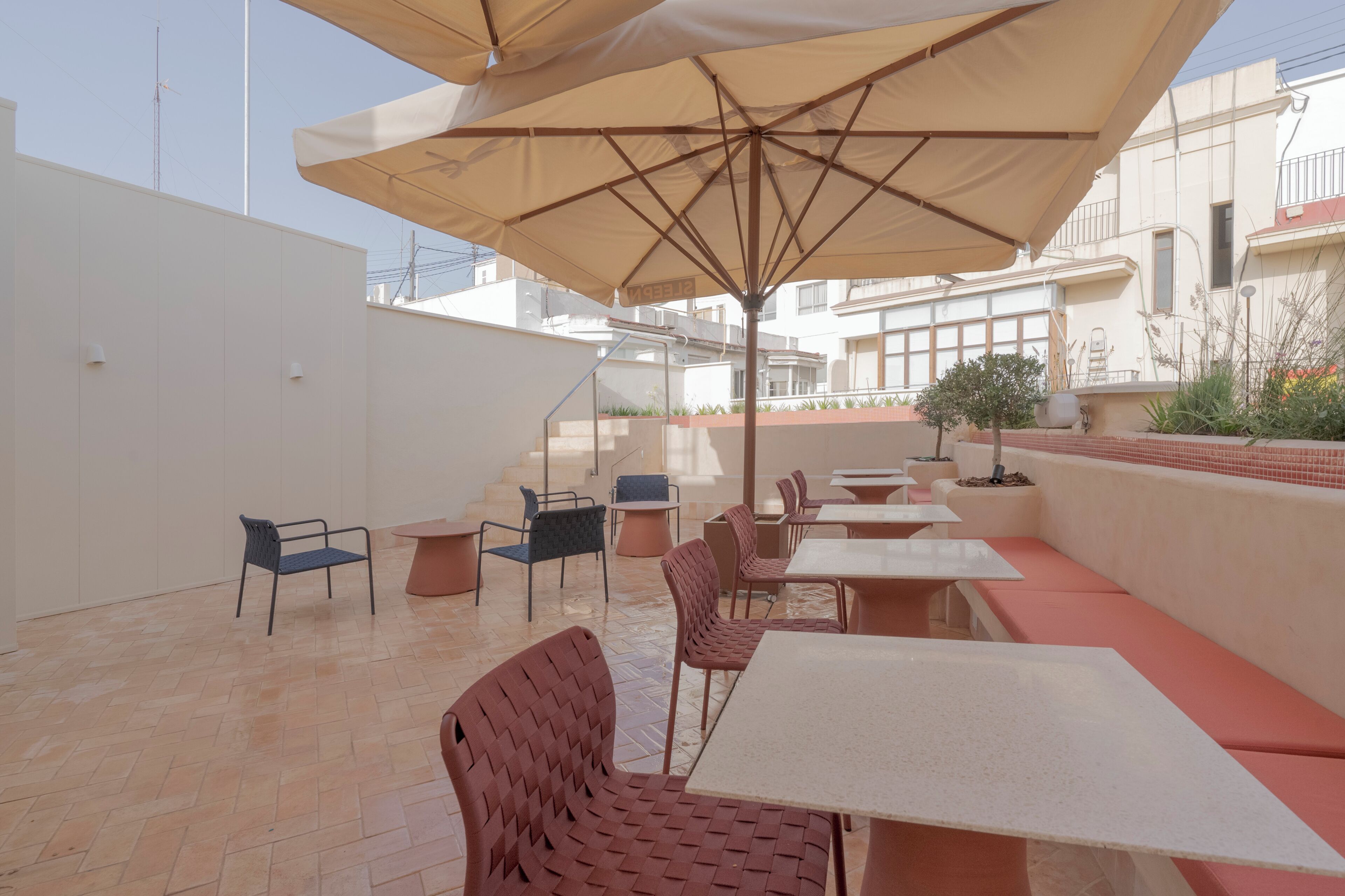 Un patio al aire libre con varias mesas y sillas, un área de estar cubierta y vistas de los edificios circundantes.