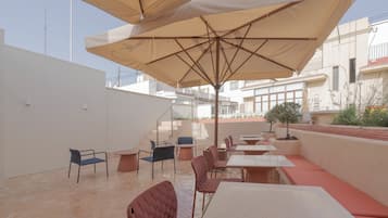 Un patio al aire libre con varias mesas y sillas, un área de estar cubierta y vistas de los edificios circundantes.