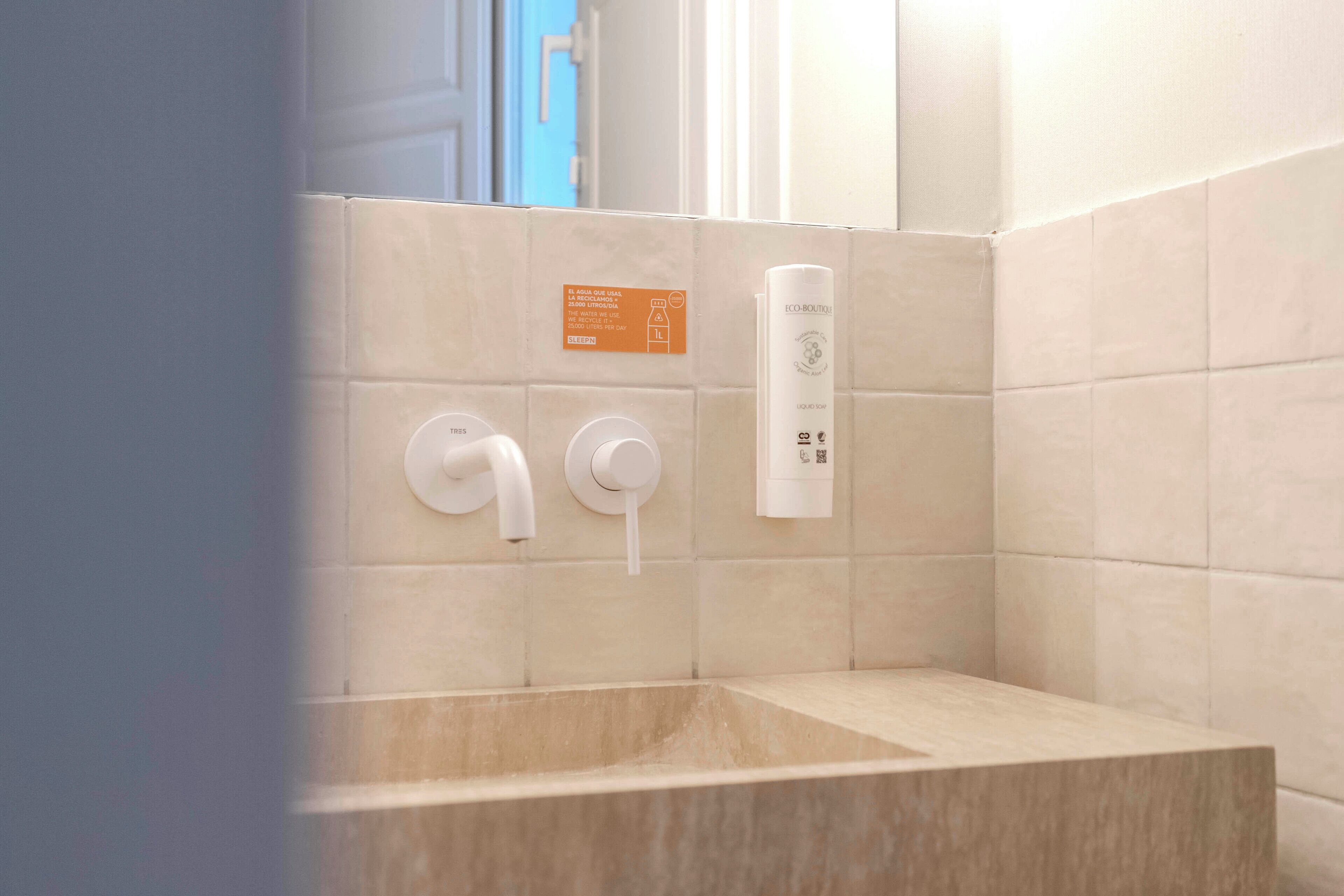 A bathroom with a beige tiled wall, a white towel dispenser, and a white bottle on the wall.