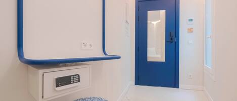 Un pasillo con una puerta azul, un banco blanco y un panel de control en la pared.