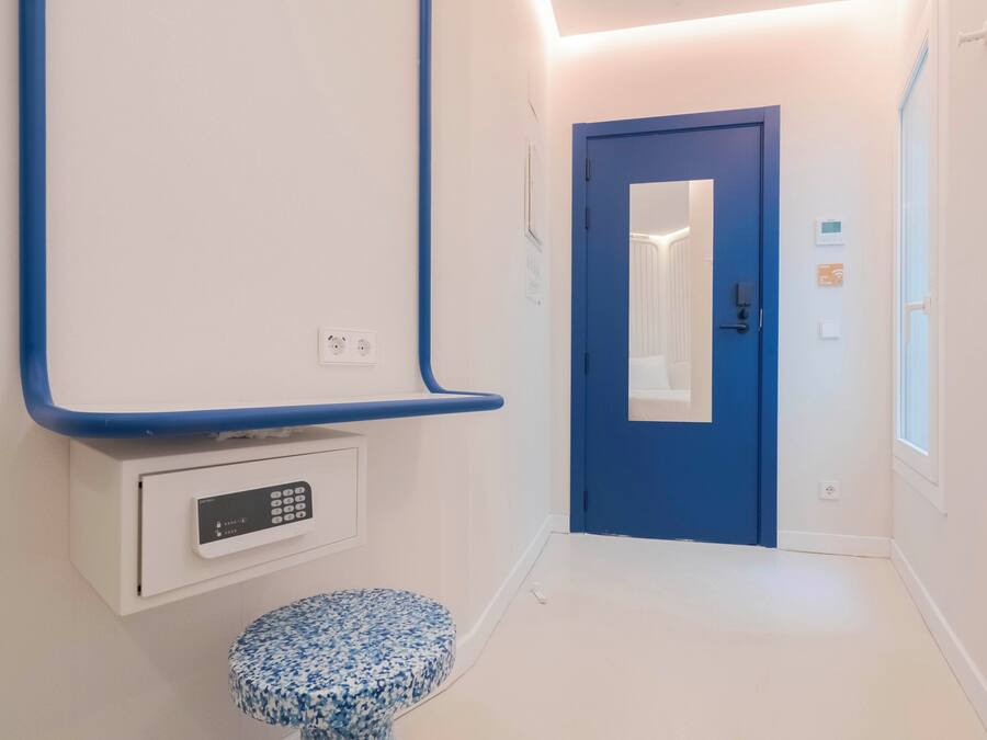 Un pasillo con una puerta azul, un banco blanco y un panel de control en la pared.