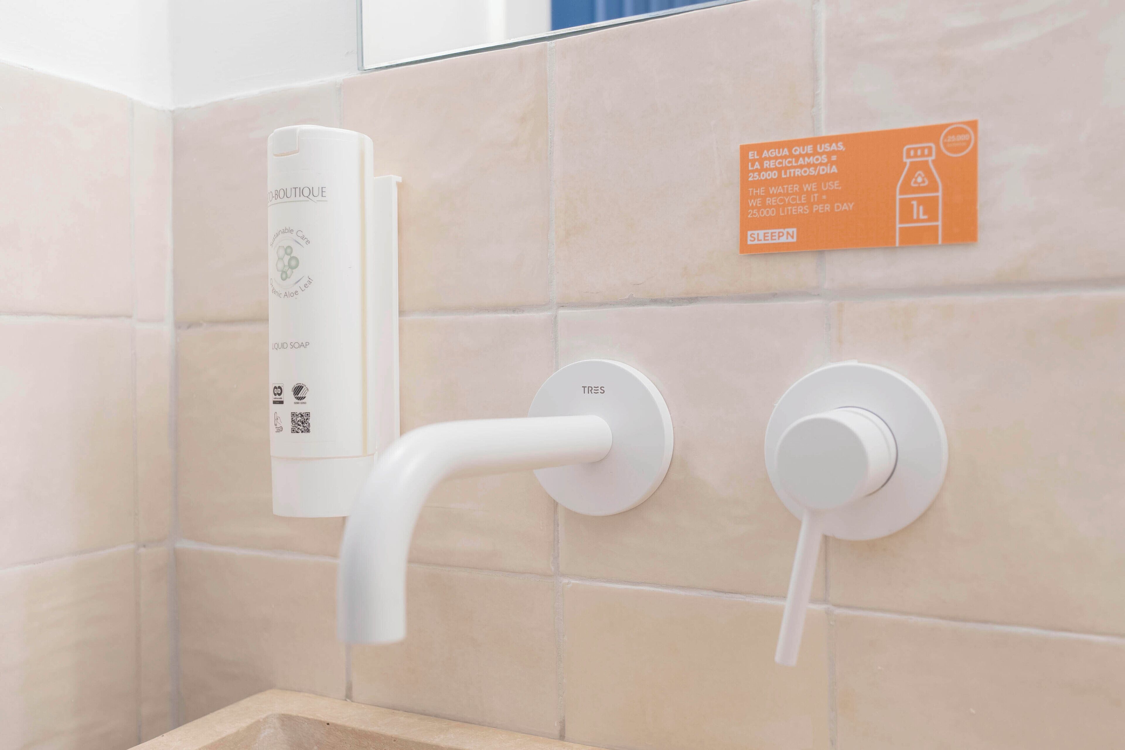 A bathroom with a hand soap dispenser, a water tap, and a recycling sign.