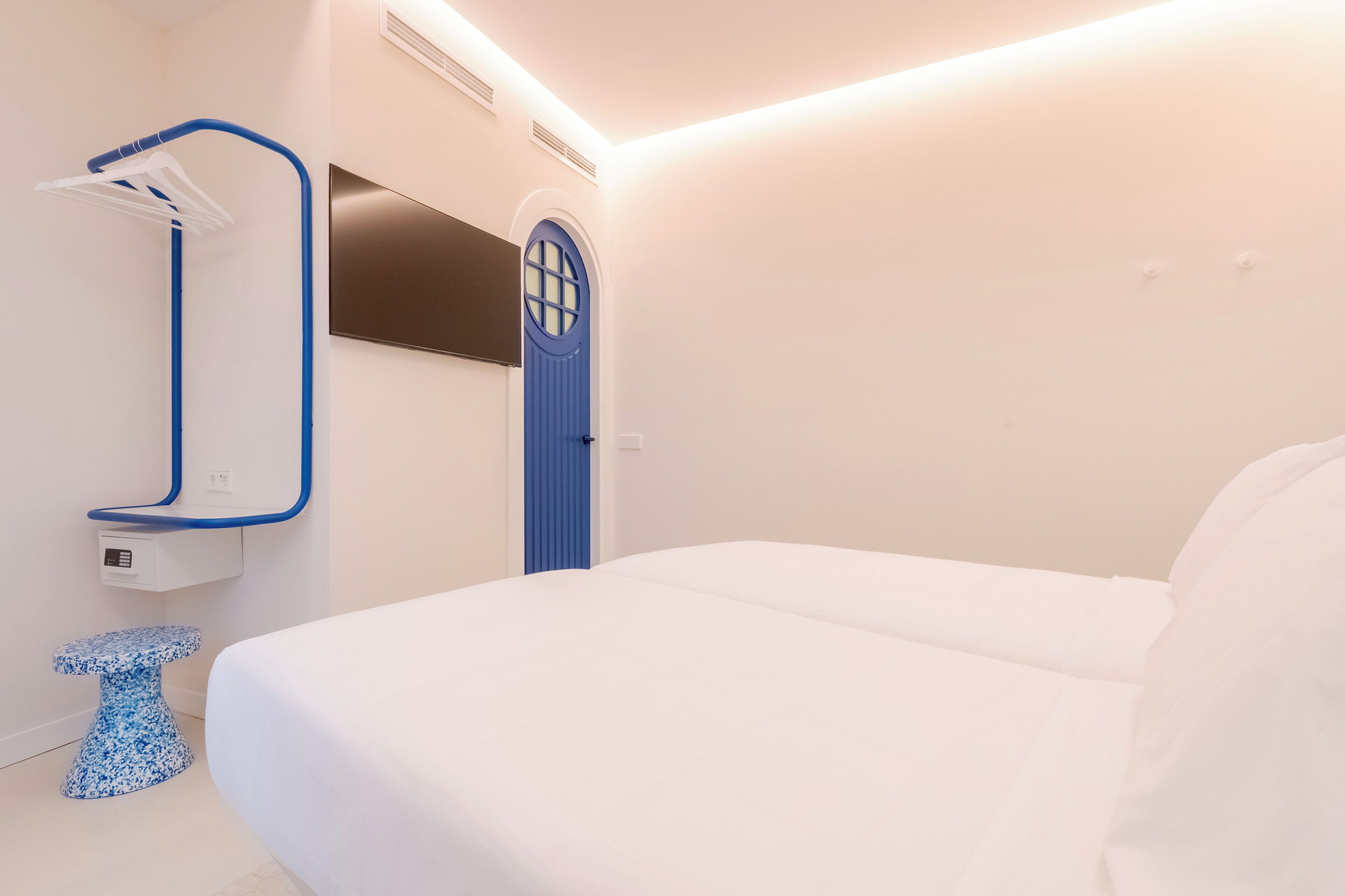 Habitación de hotel moderna con cama, una puerta azul, televisor montado en la pared y un toallero azul.