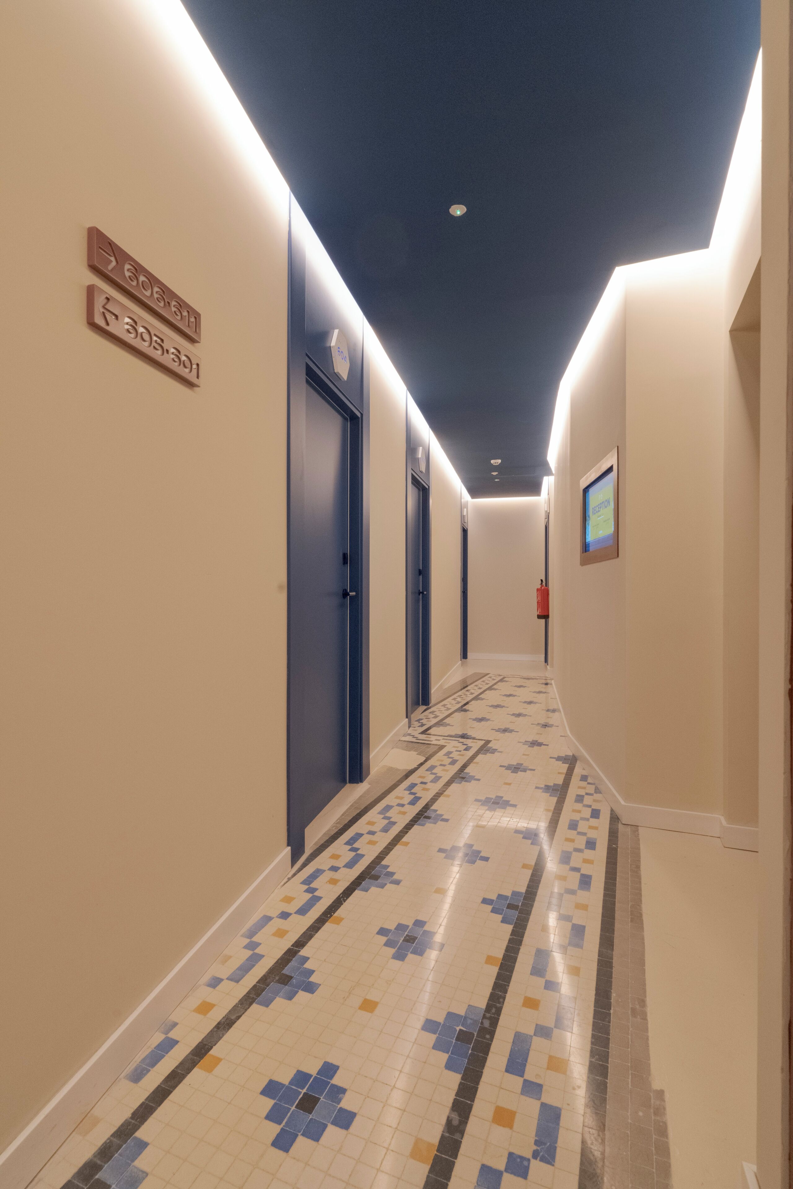 Een hotelhal met richtingaanwijzingen, een versierde vloer en een scherm dat 'RECEPTION' toont.