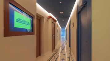 Un couloir d’hôtel avec un écran numérique sur le côté gauche, un sol à motifs et des portes de part et d’autre.