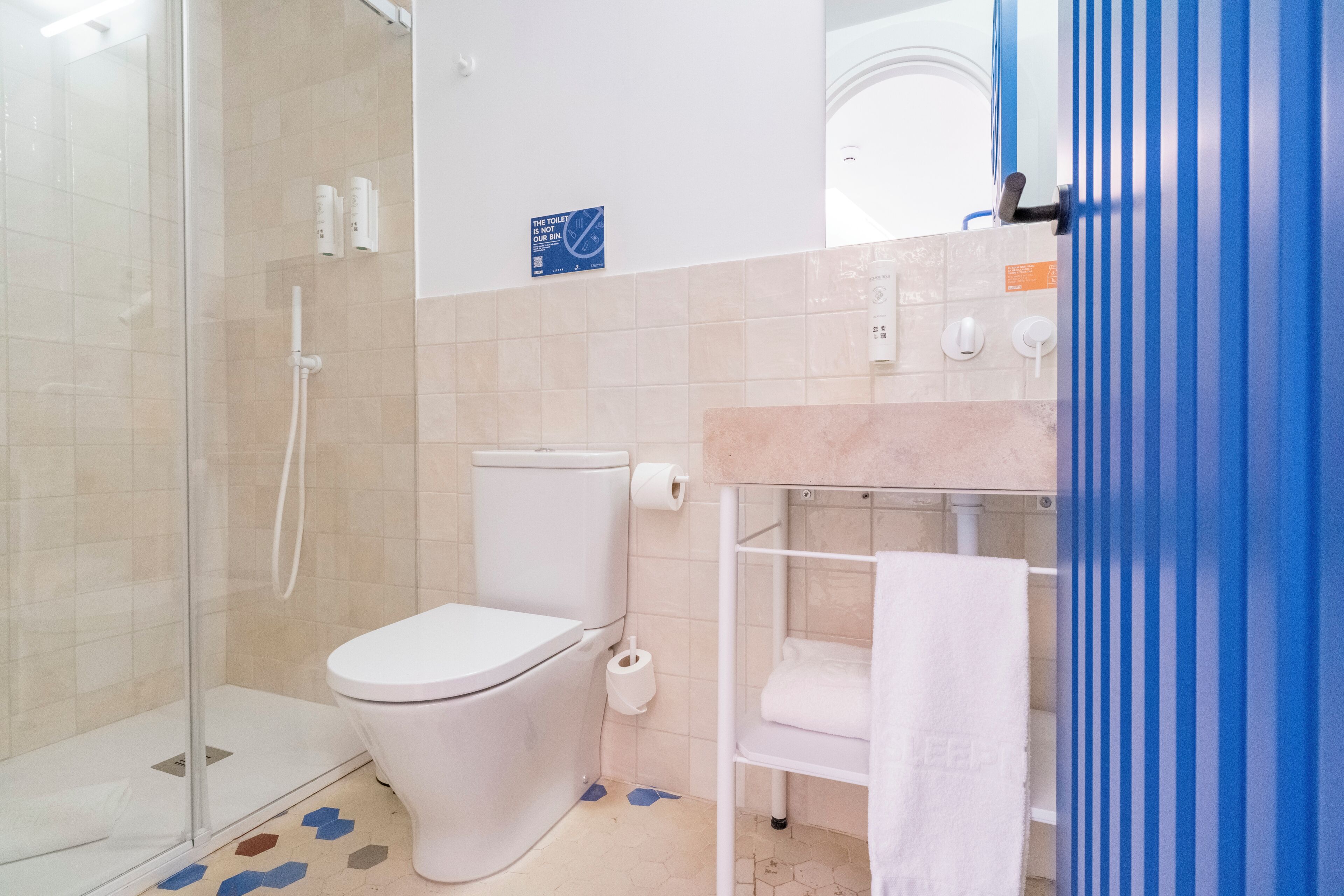 Un baño con cabina de ducha de vidrio, inodoro y lavamanos con barra para toallas.