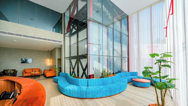 Eine moderne Lobby mit einer gebogenen, blauen Couch, einem hölzernen Empfangstresen und einer großen Glasschrankwand.