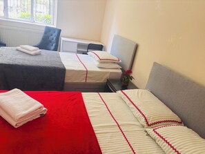 A hotel room with two beds, a red and white striped bedspread, a grey headboard, and a window with a view of greenery outside. - Samira’s home (London)