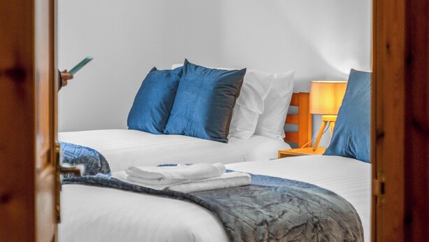 Ein Schlafzimmer mit einem Holzbettgestell, weißer Bettwäsche und blauen Kissen.
