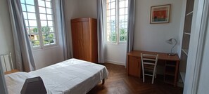 Ein Schlafzimmer mit einem Bett, einem Holzschrank, einem Schreibtisch mit Stuhl und einem Fenster mit Vorhängen.