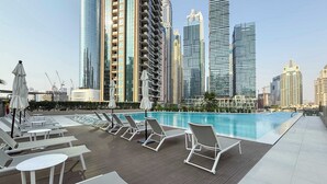 A rooftop pool area with lounge chairs and tables, surrounded by high-rise buildings. - Luxury 1BR LIV Marina Modern with Marina View (Dubai)