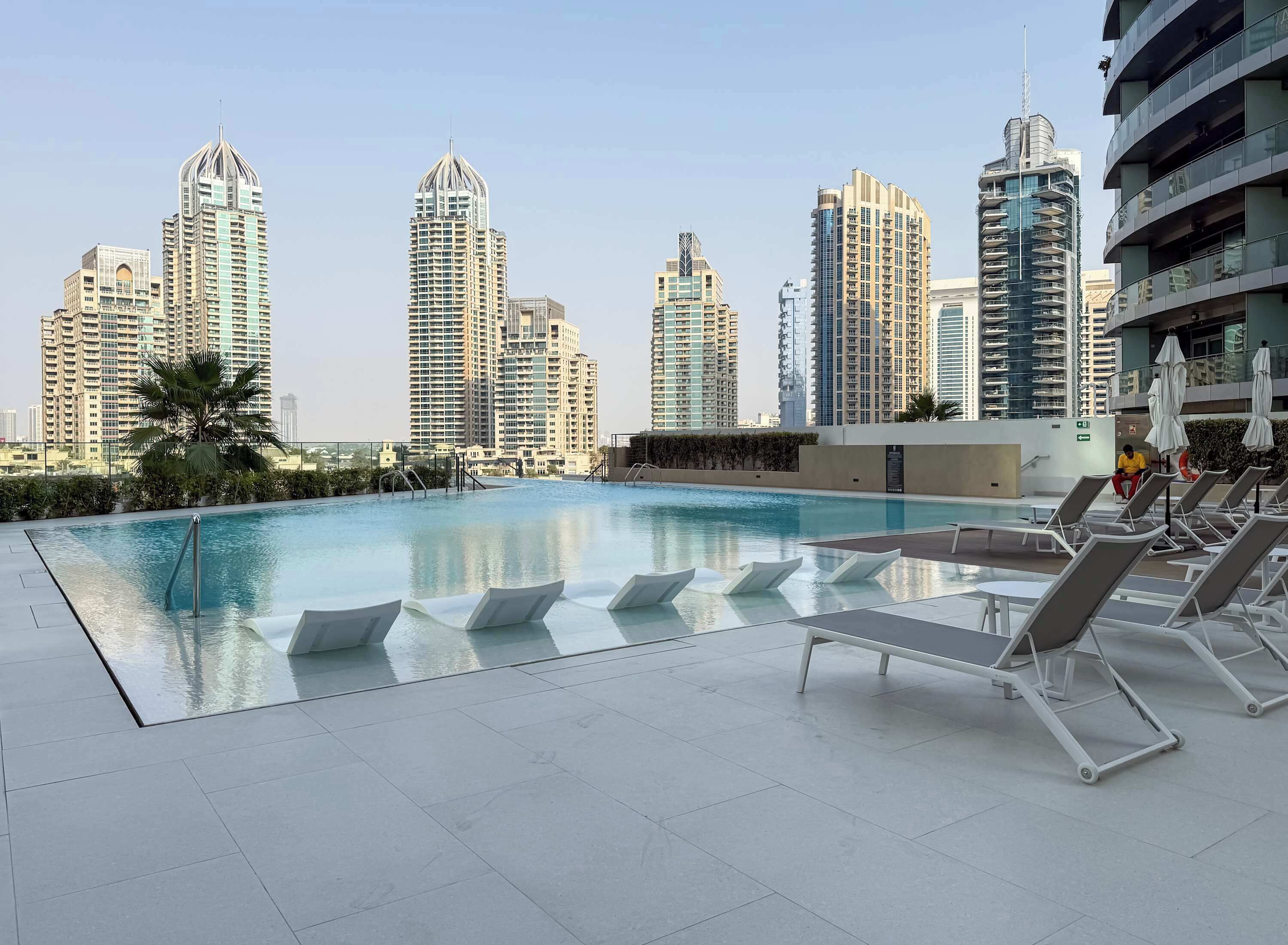 A rooftop pool with lounge chairs and a city skyline in the background.