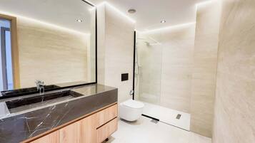 Une salle de bain moderne avec un grand miroir, un lavabo en marbre, des toilettes et une cabine de douche en verre.