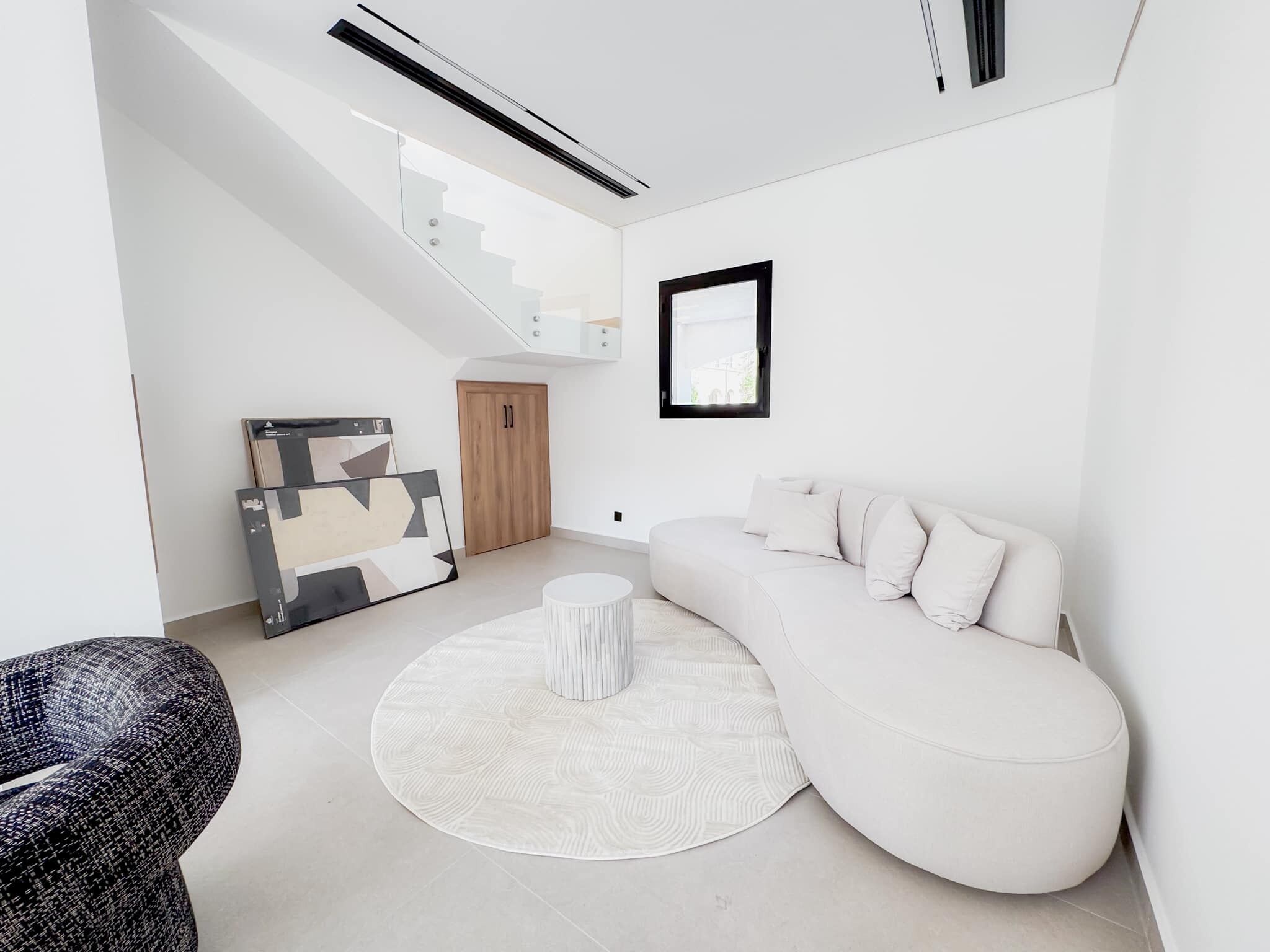 Un salon moderne avec un canapé blanc, une table basse ronde et un escalier menant à un niveau supérieur.