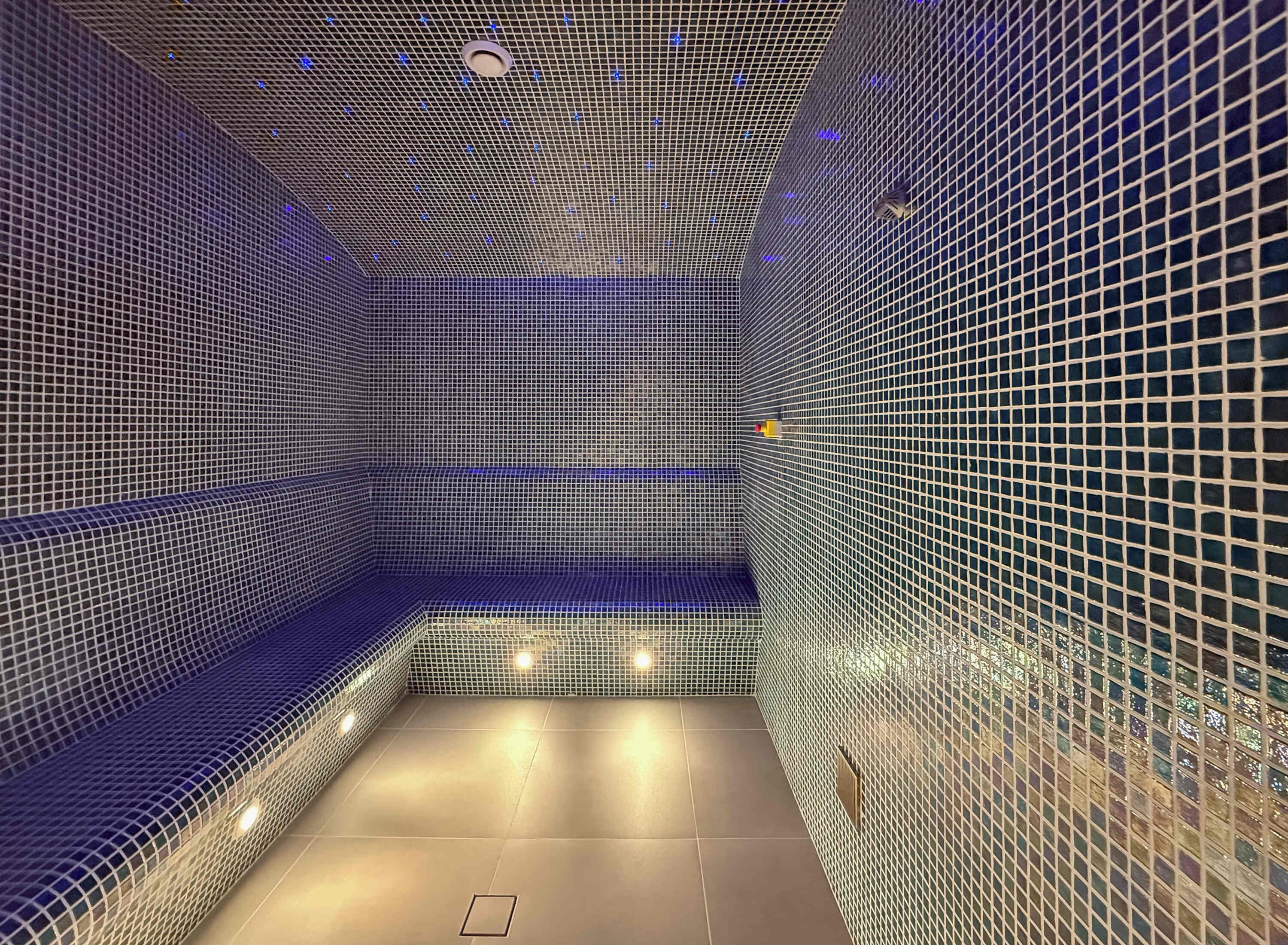 Un espace moderne et clos, doté d’un plafond et de murs à motifs géométriques, avec un luminaire central et un petit objet rond placé sur le mur de droite.
