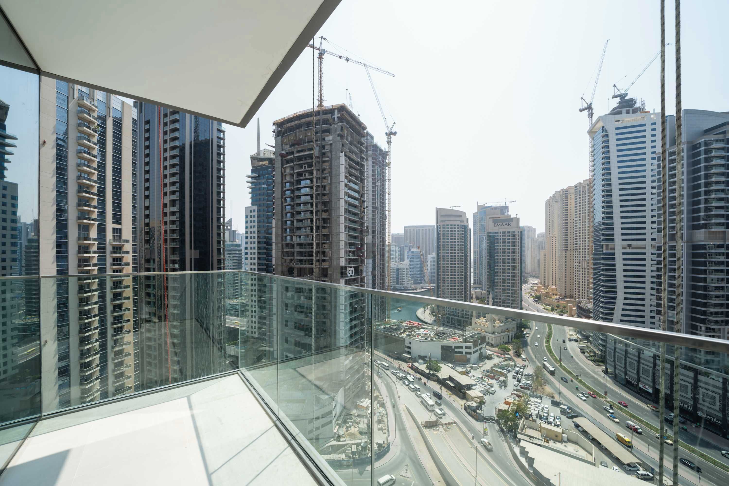 Um edifício alto com varanda de vidro com vista para uma área urbana movimentada, com várias guindastes e edifícios altos.