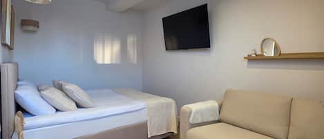 A modern bedroom with a bed, a sofa, a TV, and a wooden floor.