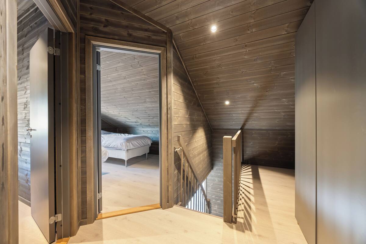 A modern loft bedroom with a sloped ceiling, a wooden staircase, and a bed with white bedding.