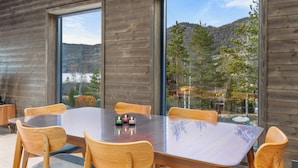 A modern wooden interior with a large dining table and chairs, large windows offering a view of a forested hillside. - Berre Veit 6p (Kviteseid)