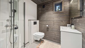 A modern bathroom with a glass-enclosed shower, a toilet, and a sink with a wooden wall backdrop. - Berre Veit 6p (Kviteseid)