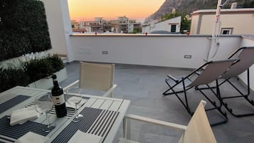 Una terrazza sul tetto con un tavolo apparecchiato per due, una sedia e una bottiglia di vino.
