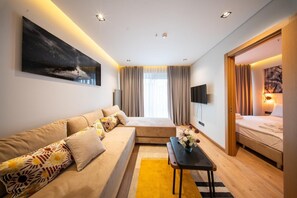 Une chambre d’hôtel moderne avec un canapé, une petite table agrémentée de fleurs, un lit, une télévision et un tableau au mur.