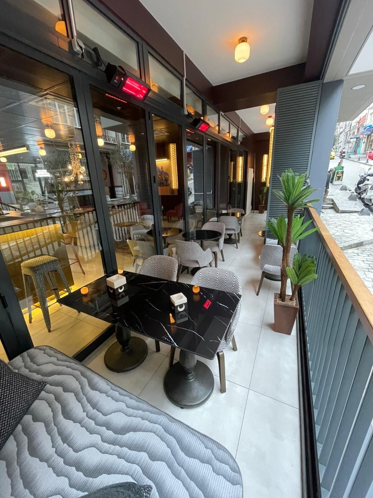 A modern outdoor seating area with tables and chairs, a potted plant, and a view of the street.