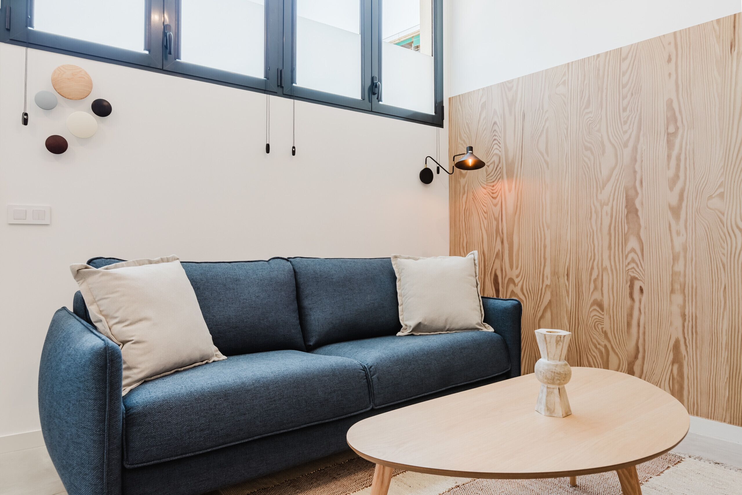 A modern living room with a blue sofa, a round wooden coffee table, and a wooden accent wall.