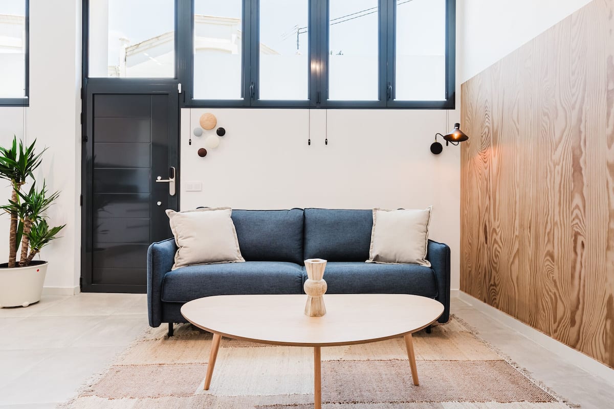 A modern living room with a blue sofa, a round coffee table, a wooden accent wall, and a potted plant.